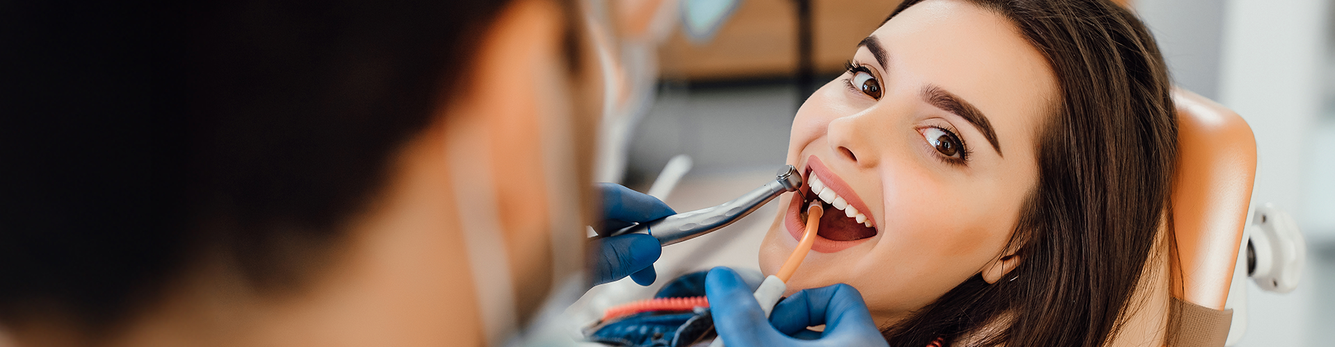 Gloved hands using dental tools in girl's mouth.